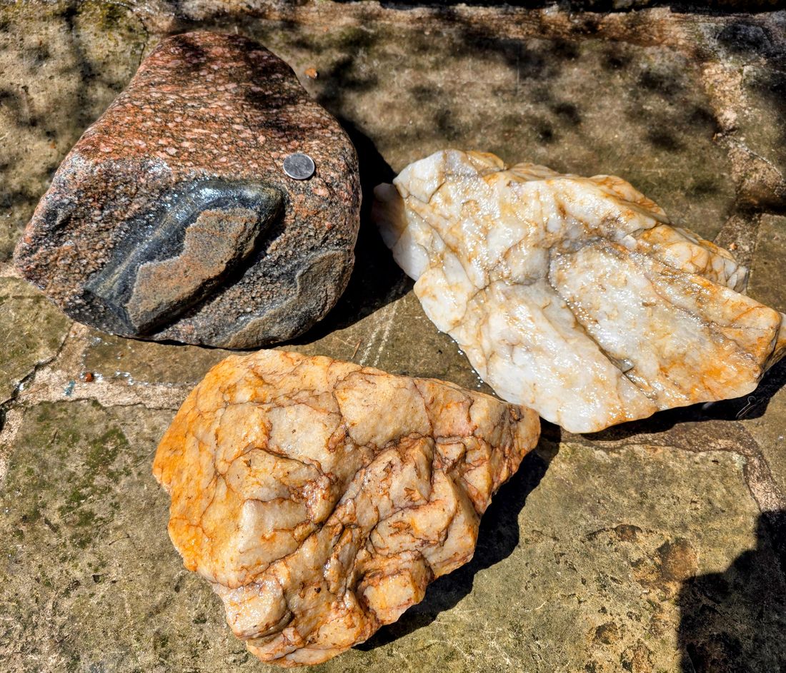 A granite boulder with a quarter for scale, next to pieces of vein quartz.
